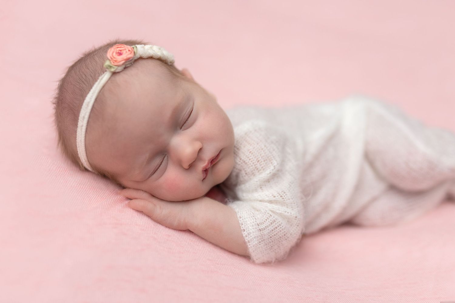 Newborn baby girl sleeping peacefully in knit romper with flower headband, posed by Pamela Clark, Cedar Park newborn photographer