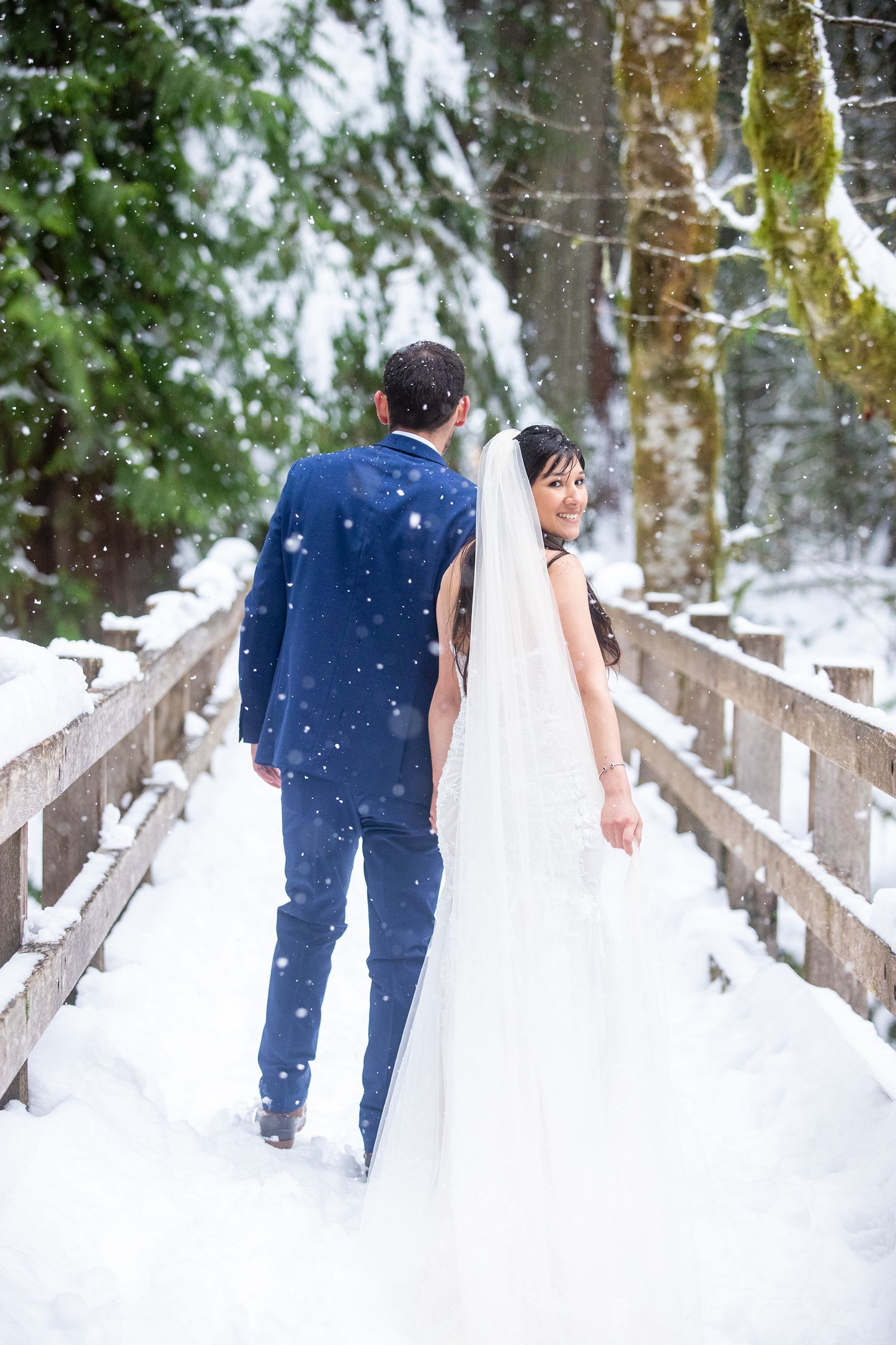 Winter wedding portrait of bride and groom walking on snowy bridge, photographed by Cedar Park Photographer Pamela Clark