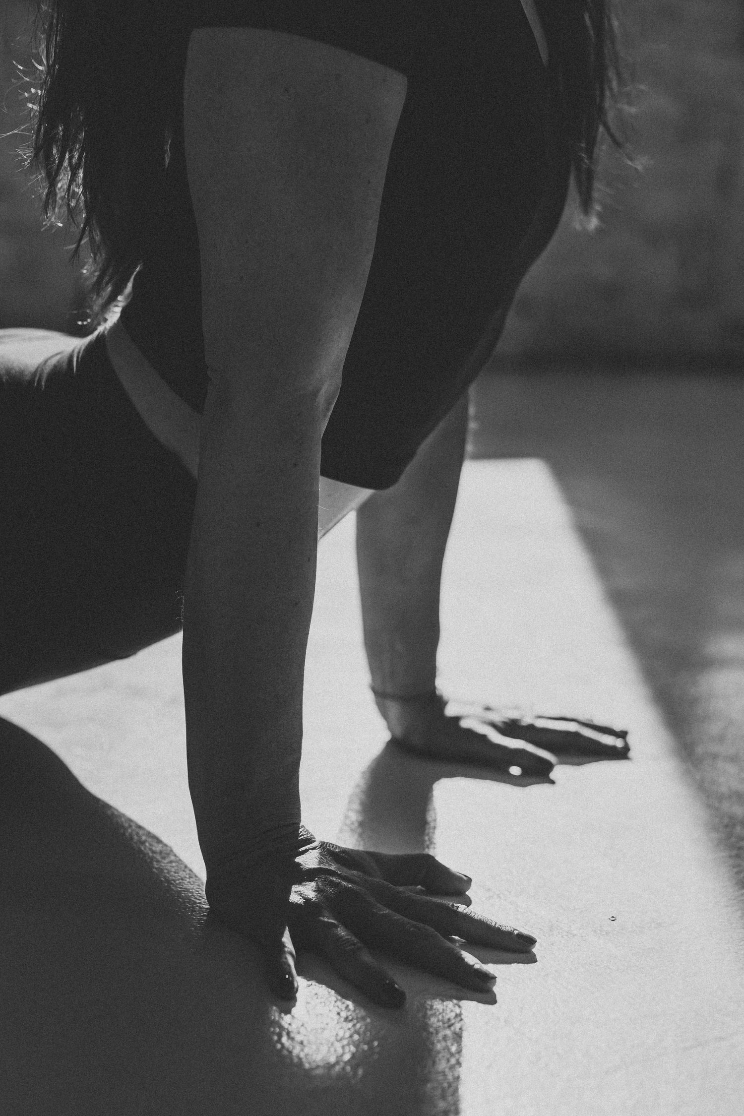 Black and white artistic photo showing hands pressed against a reflective floor surface in dramatic lighting.