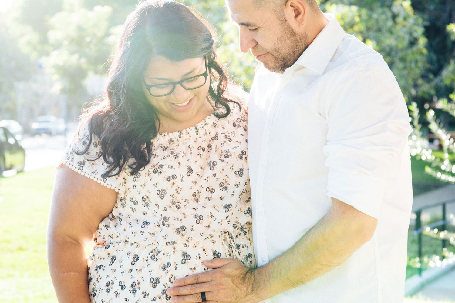 Sunlit outdoor maternity photo with expectant couple in casual attire.