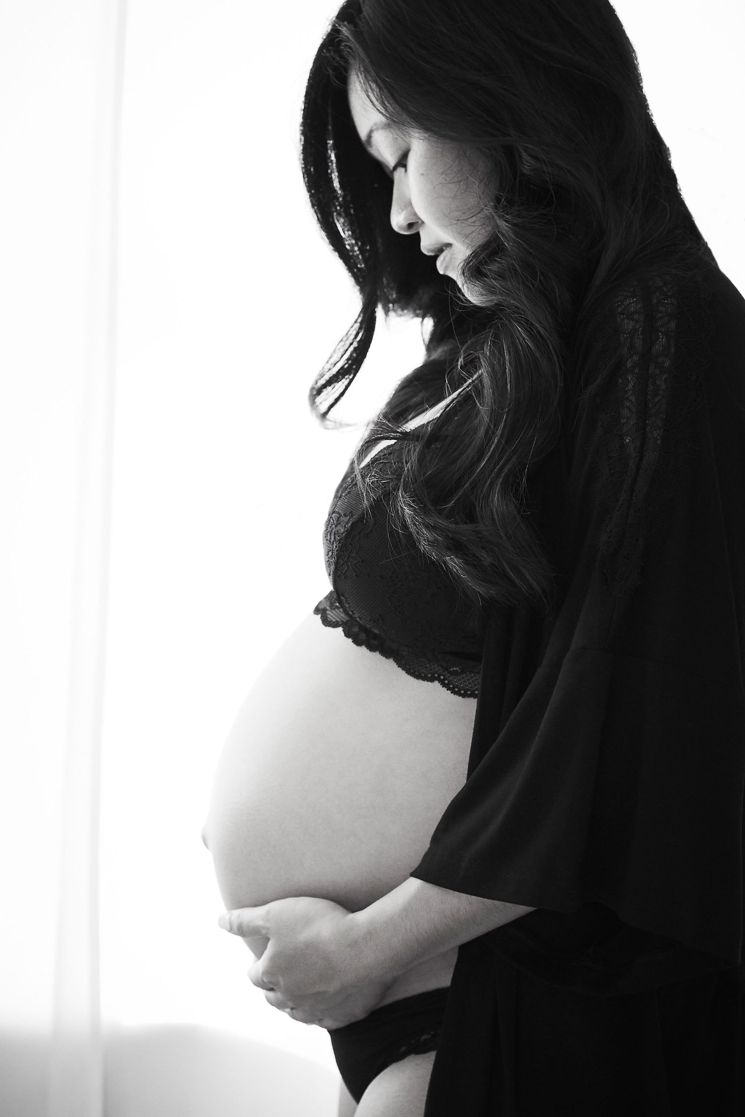 Black and white silhouette of expectant mother holding belly by window.