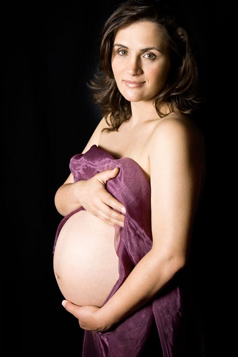 Maternity portrait showing an expectant mother draped in purple fabric against dark background.