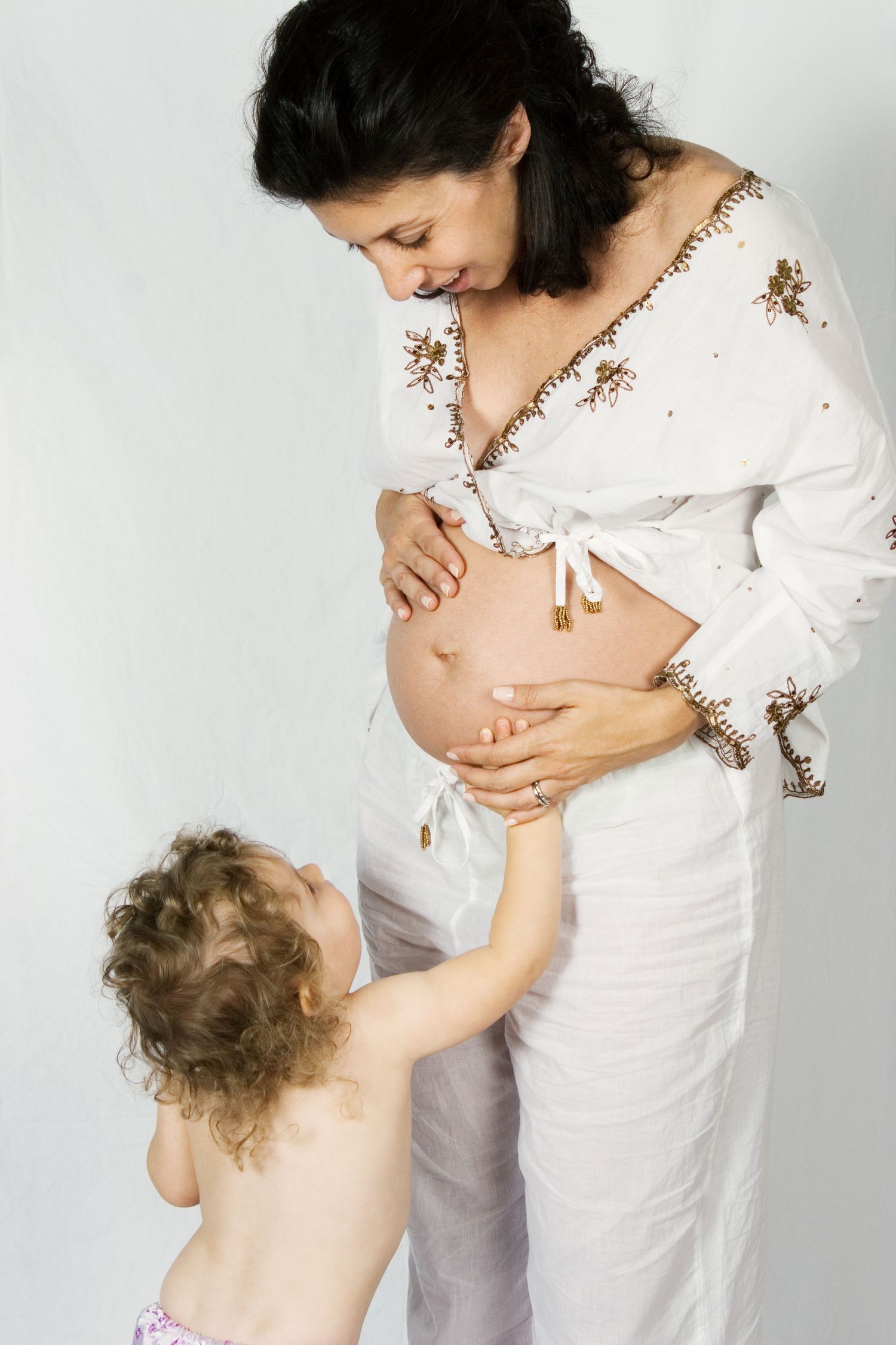 Mother in white embroidered top shares pregnancy moment with young child.