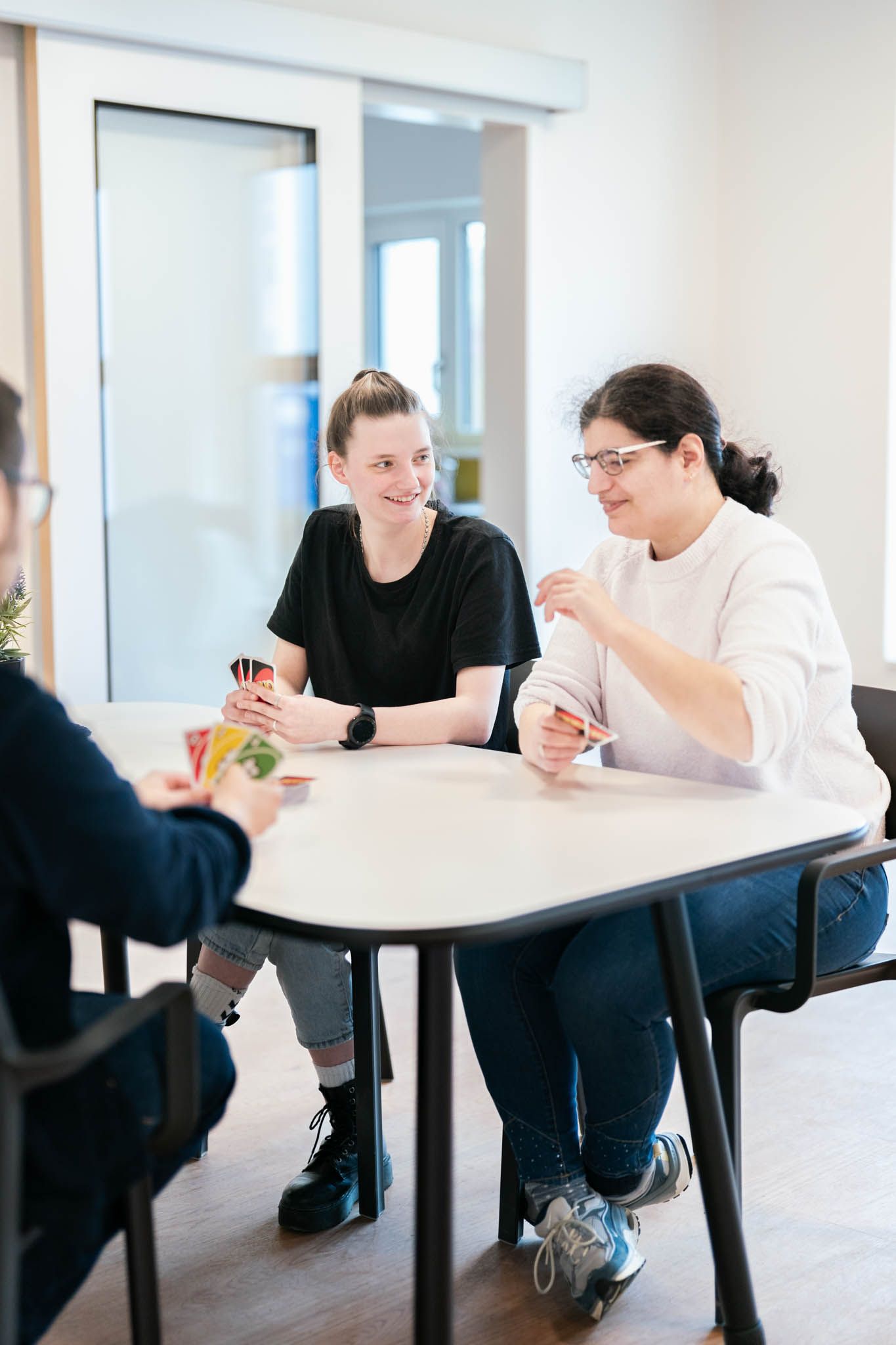 Two people sit at a round table in a bright office space having an informal meeting or discussion.