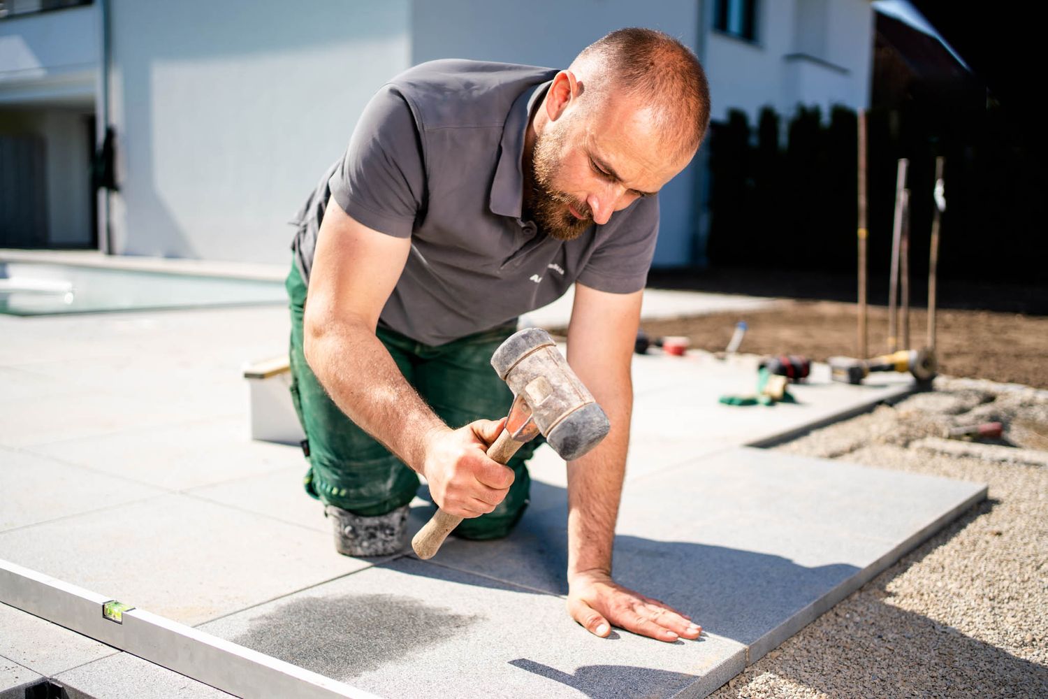 Construction worker in green overalls kneels down to carefully measure and mark a concrete surface.