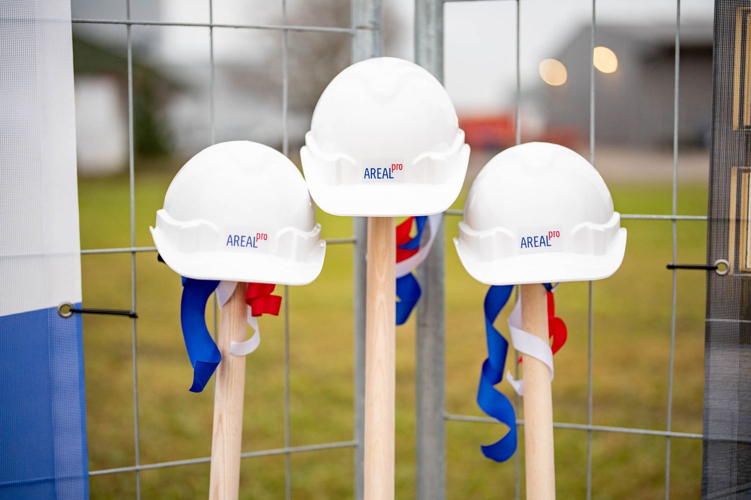 White hard hats with blue and red accents hang on a wire mesh fence in a row.