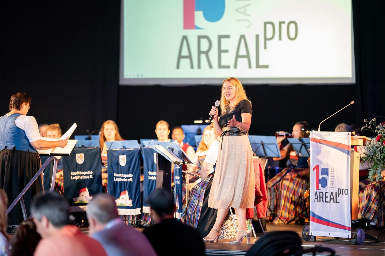 People stand on stage at a professional conference or event with presentation screens visible in the background.