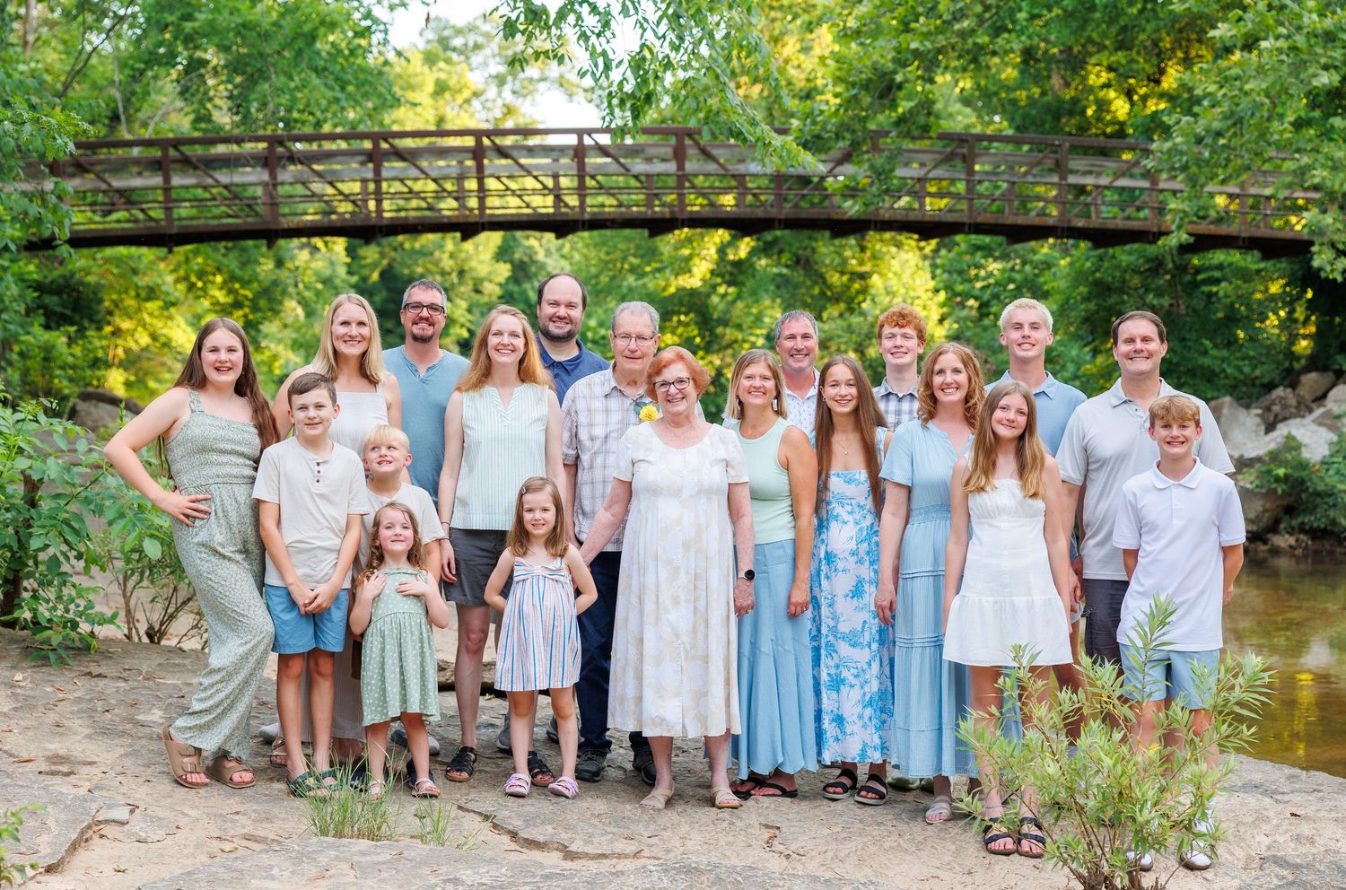 Large group in coordinating blue and white outfits poses together on rustic wooden bridge over creek in Branson, MO.