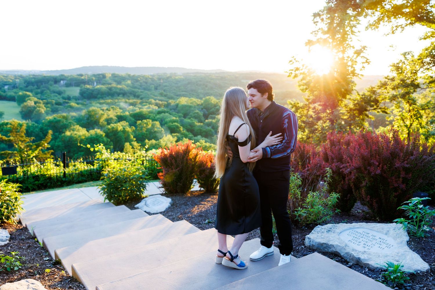 Couple sharing a romantic kiss at sunset after proposal on a garden patio with lush green hills in Branson, Missouri.