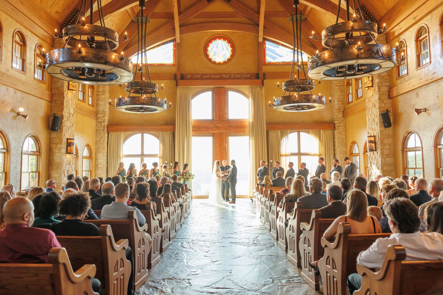 A wedding ceremony in a grand wooden chapel with high ceilings, arched windows and guests seated in wooden pews at Big Cedar Lodge.