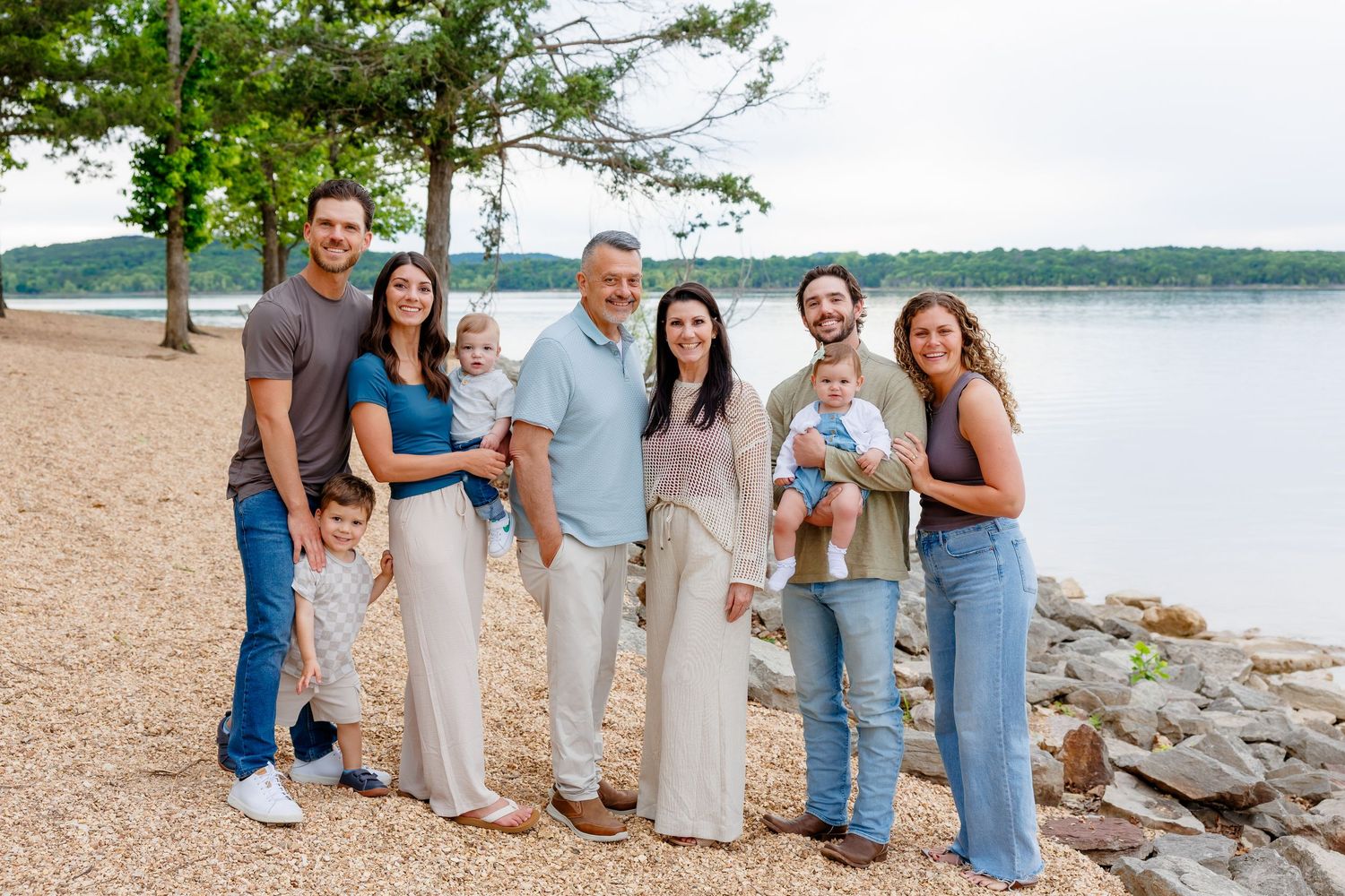 Family of eight smiling together on a scenic lakeside beach surrounded by trees at Table Rock Lake in Branson, MO.