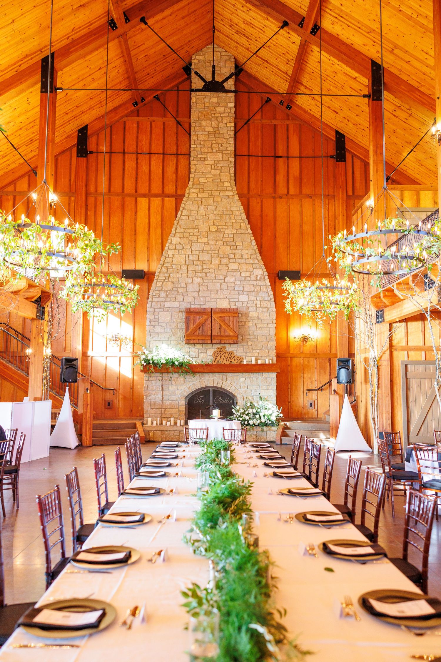 Rustic wooden barn venue with elegant table settings and stone fireplaces illuminated by twinkling string lights.