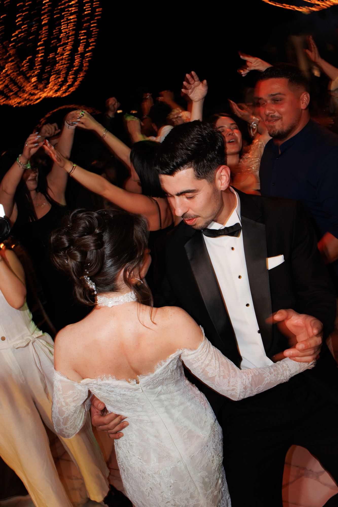 Bride and groom share first dance at wedding reception surrounded by celebrating guests in elegant evening attire.