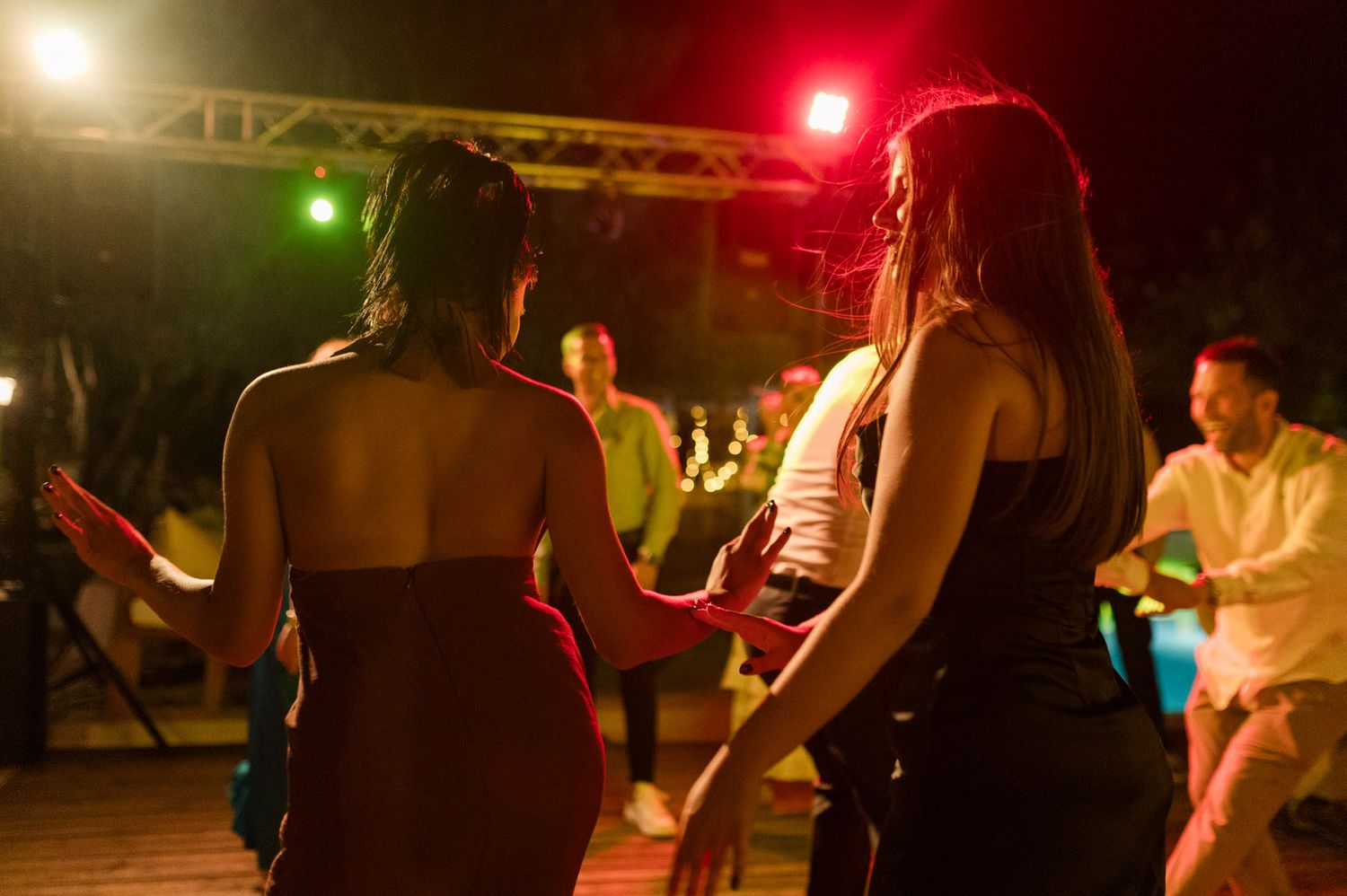 Two women dancing at an outdoor night party with colorful stage lights illuminating the festive scene.
