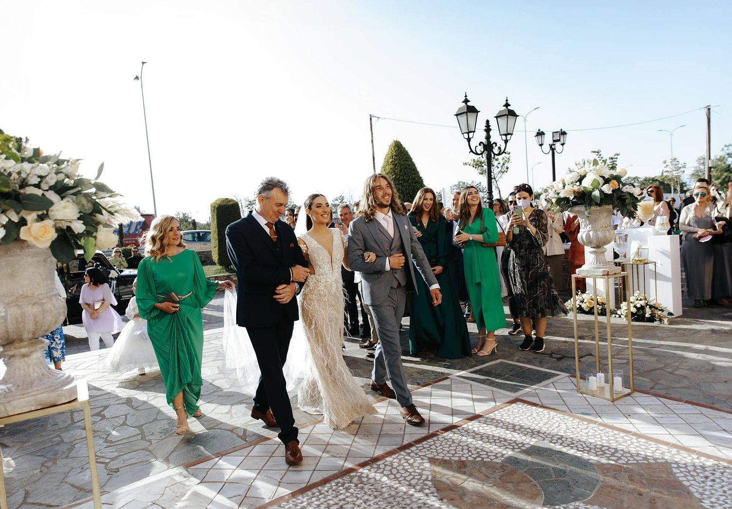 Wedding party in emerald green dresses and formal attire dance together on a paved outdoor courtyard during celebration.