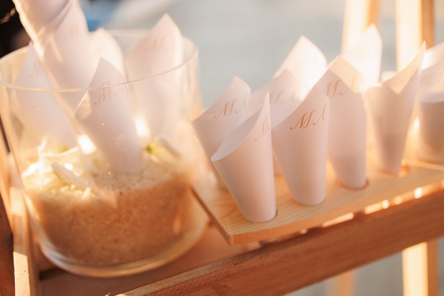 White paper cones filled with rice displayed on a wooden rack for a wedding ceremony send-off.