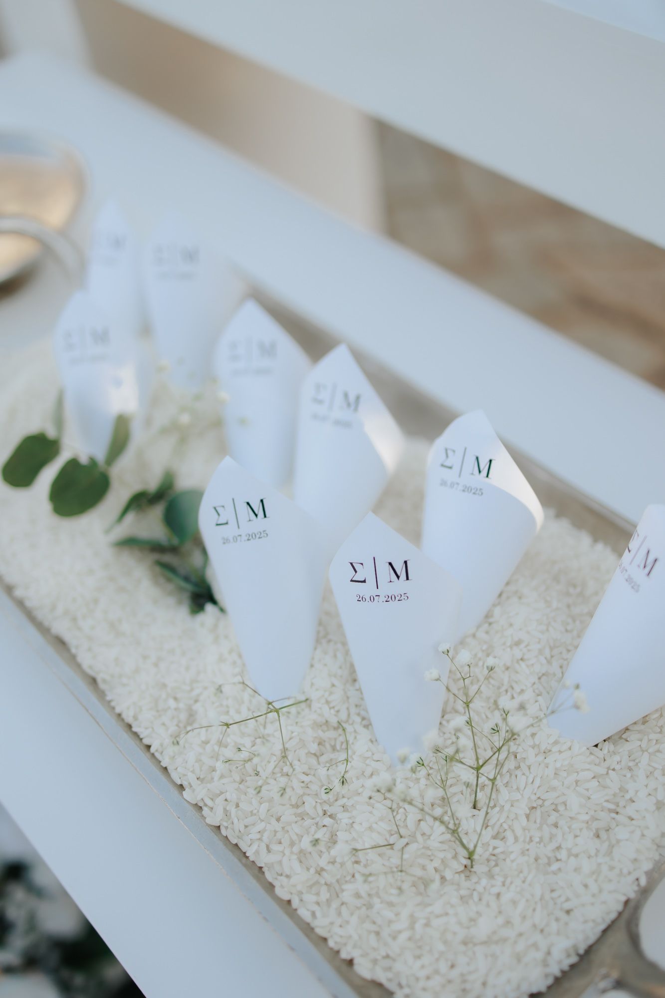 Elegant wedding paper cones with monogram S|M displayed in white rice with baby's breath on a white bench.