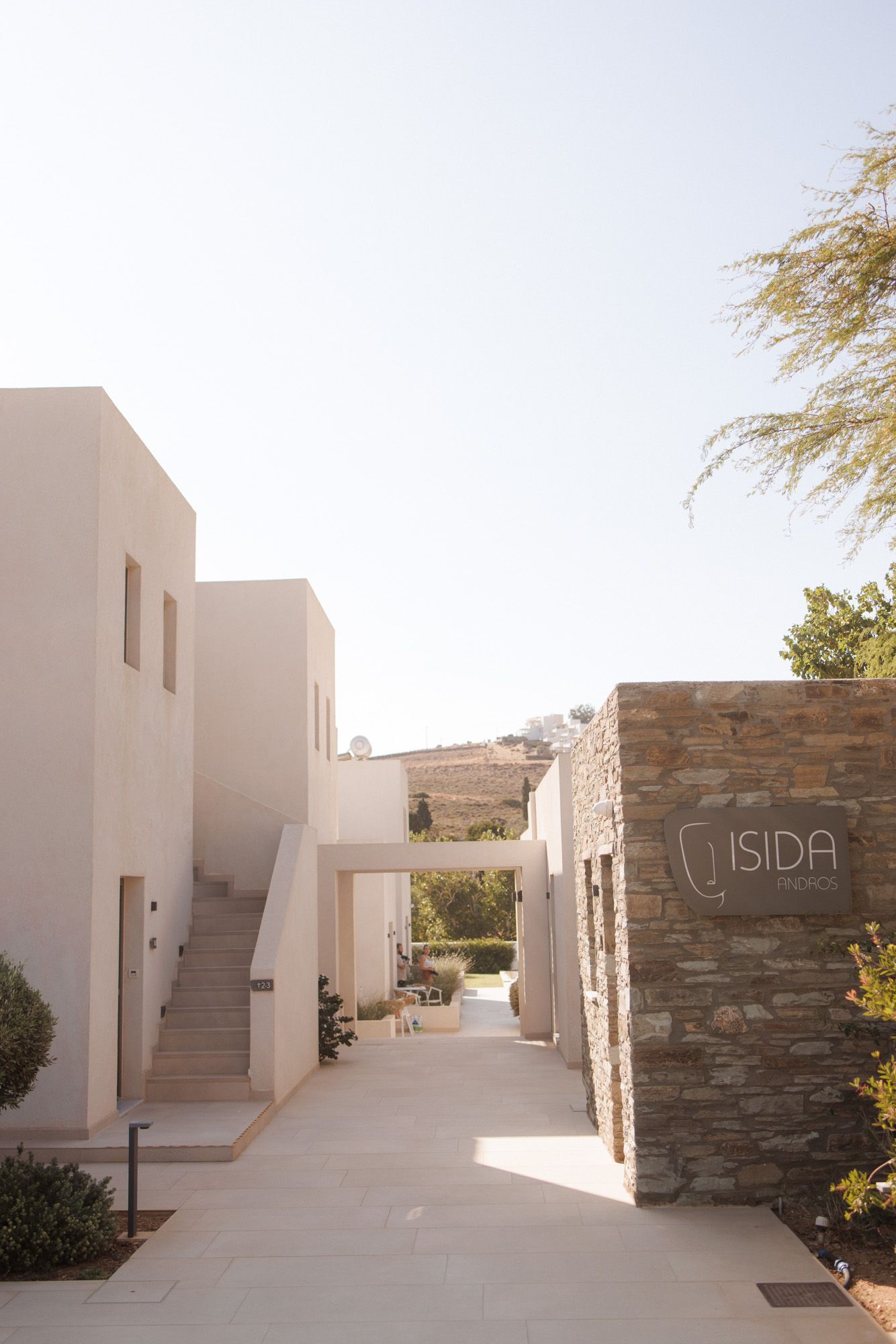Entrance pathway of Isida hotel with white minimalist architecture and stone wall signage.