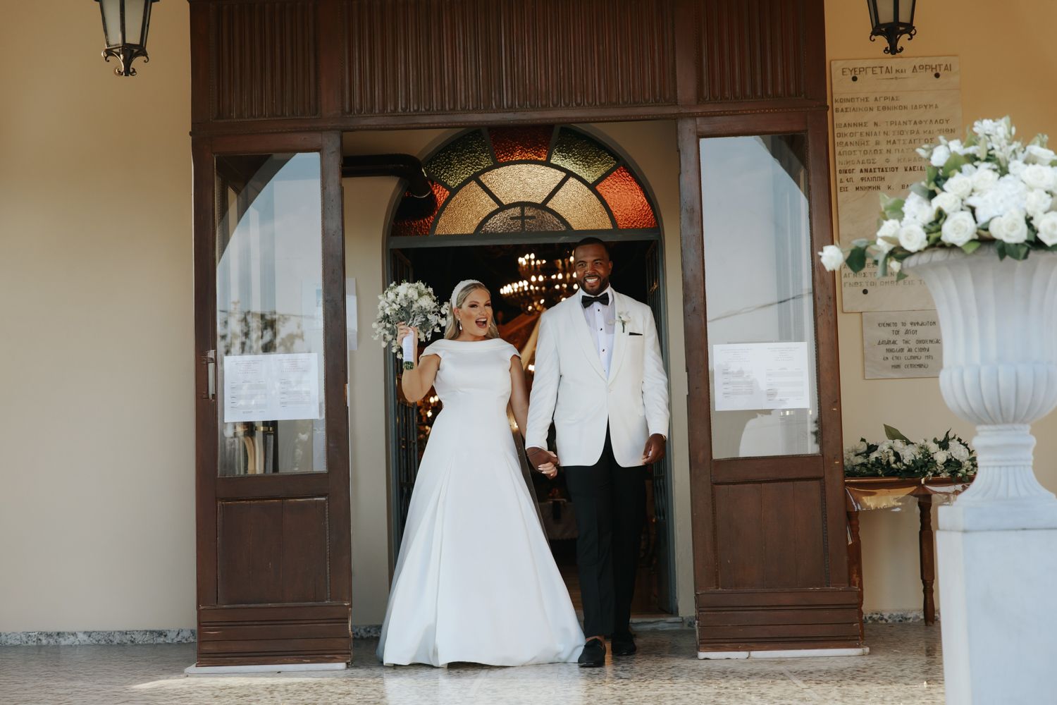 Newlywed couple holding hands and smiling as they exit church doors after wedding ceremony.