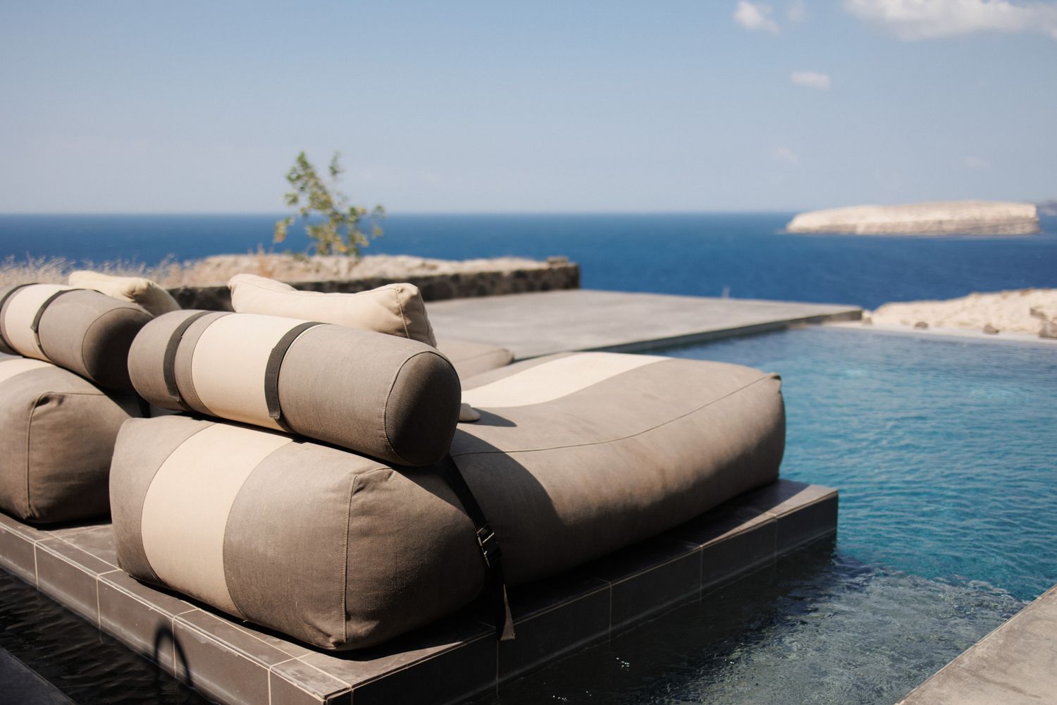 Luxurious infinity pool lounge chairs with striped cushions overlooking the deep blue Mediterranean Sea.