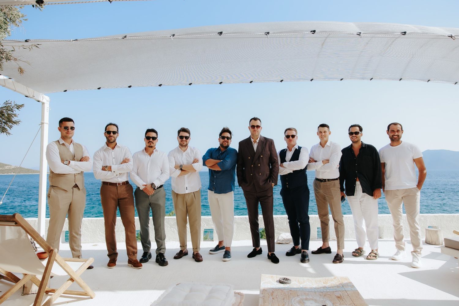 Group of groomsmen posing together on a white outdoor terrace with a beautiful blue sea backdrop.