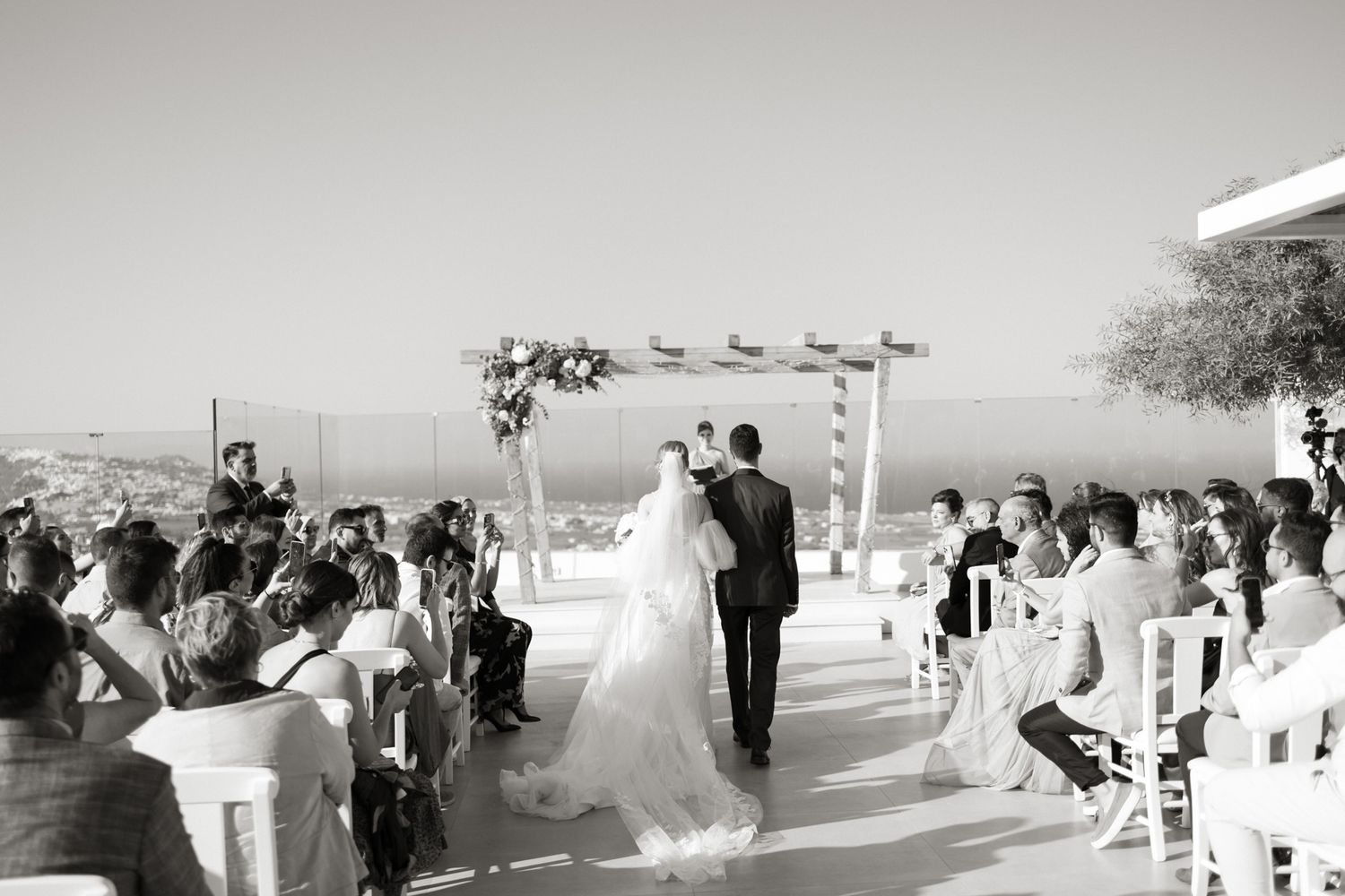 Black and white photo of an outdoor wedding ceremony with sea view in Santorini Greece.