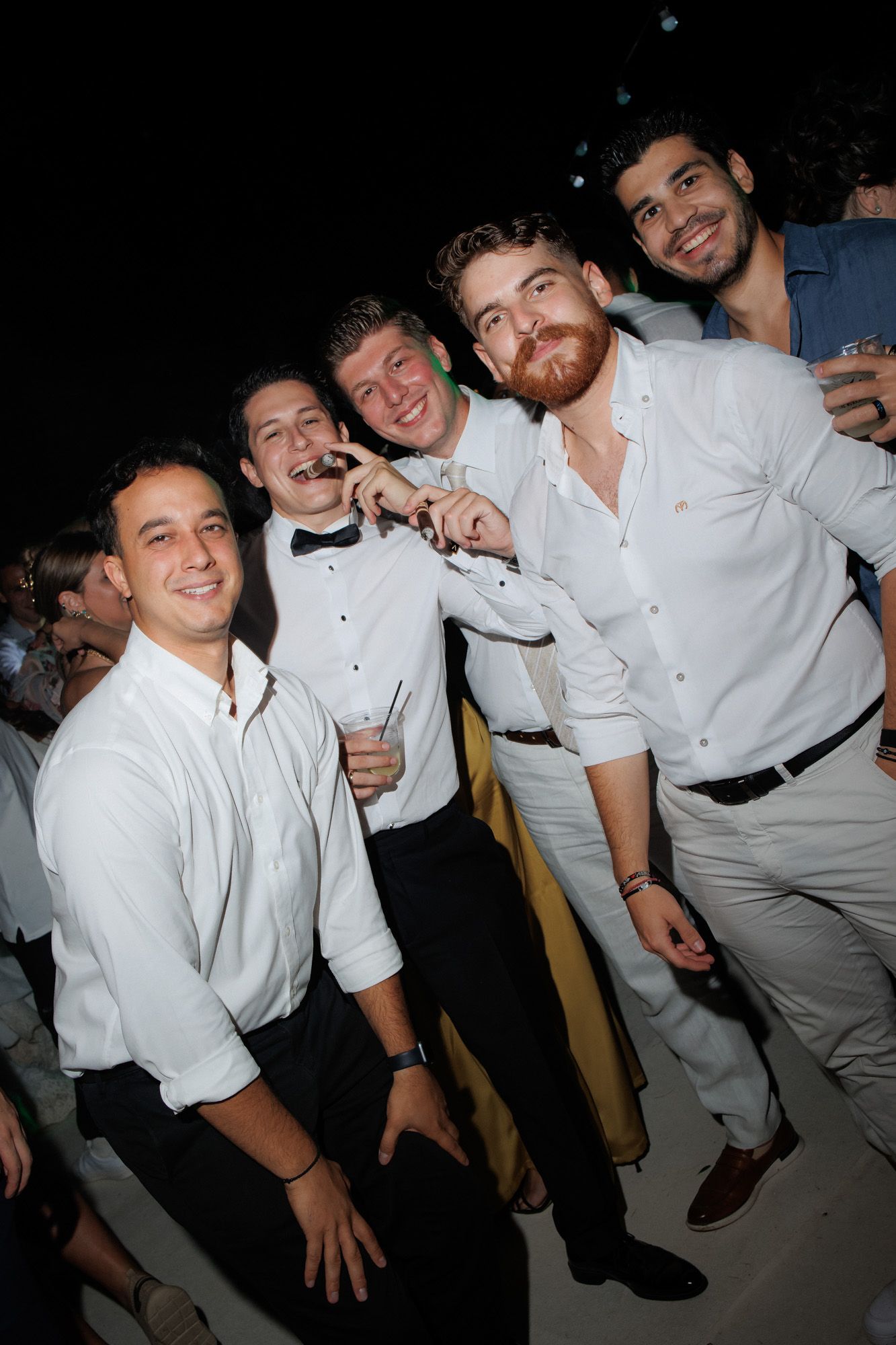 Group of five men in white shirts smiling and posing together at wedding reception.