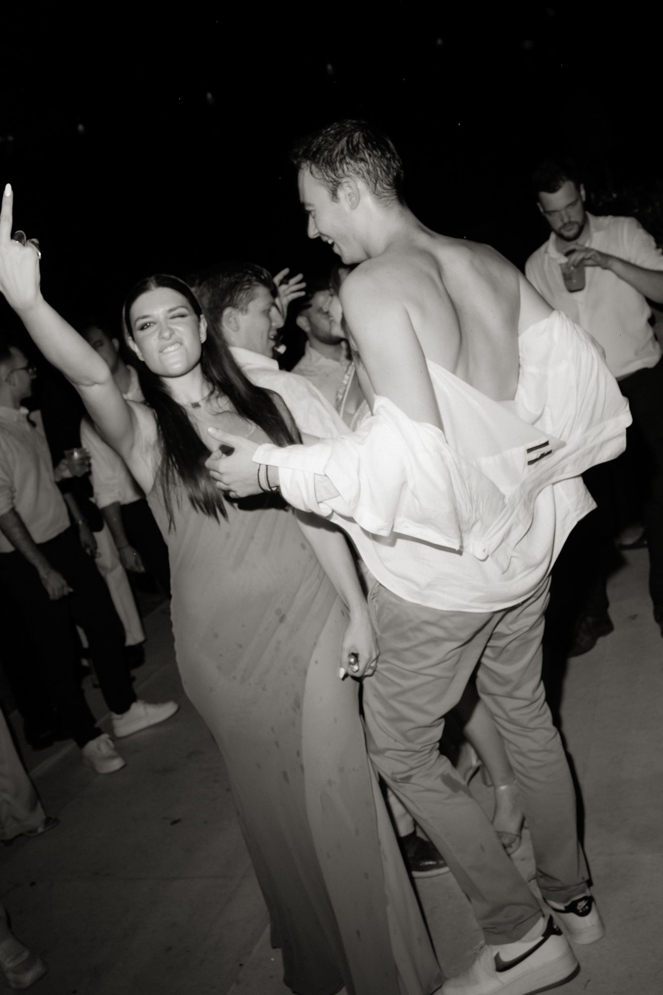 Black and white photo of guests dancing energetically at an outdoor wedding reception party at night.