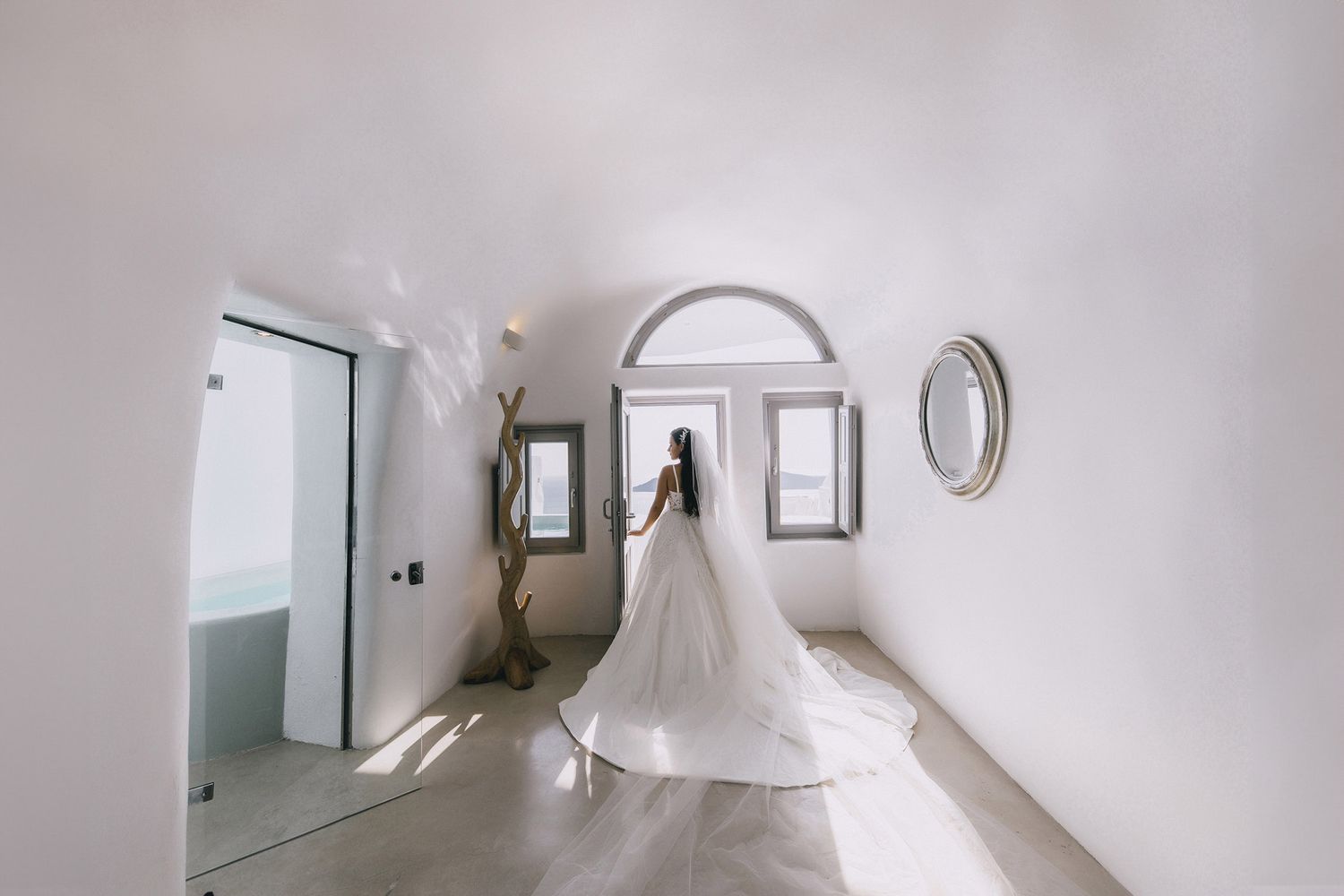 Elegant white wedding dress silhouette standing in minimalist hallway with arched window and framed artworks.