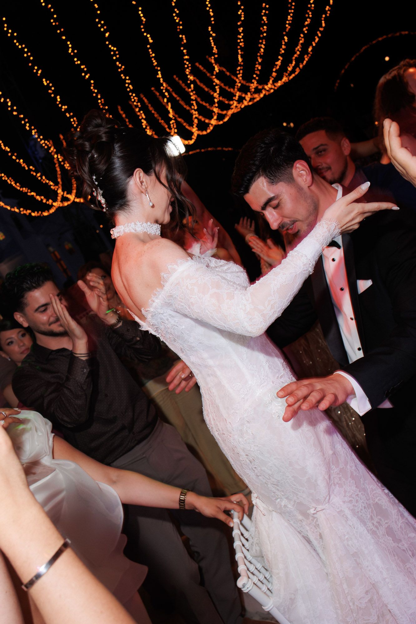 Bride and groom share first dance at elegant wedding reception with fairy lights overhead.