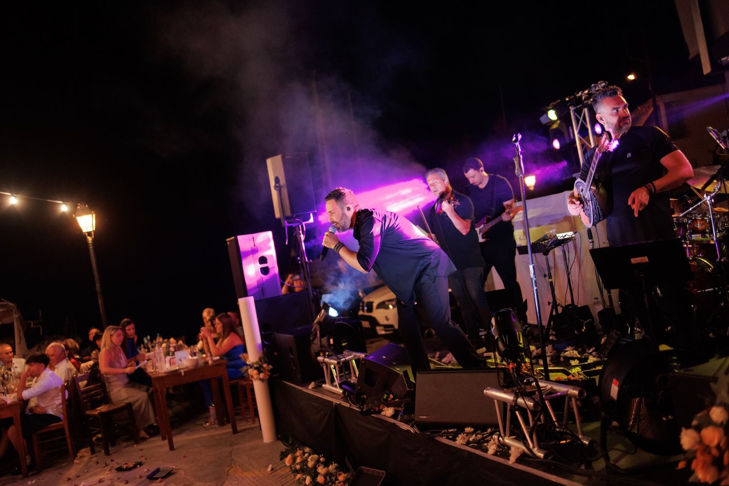 Energetic live band performs on illuminated stage with purple lights at outdoor wedding reception.
