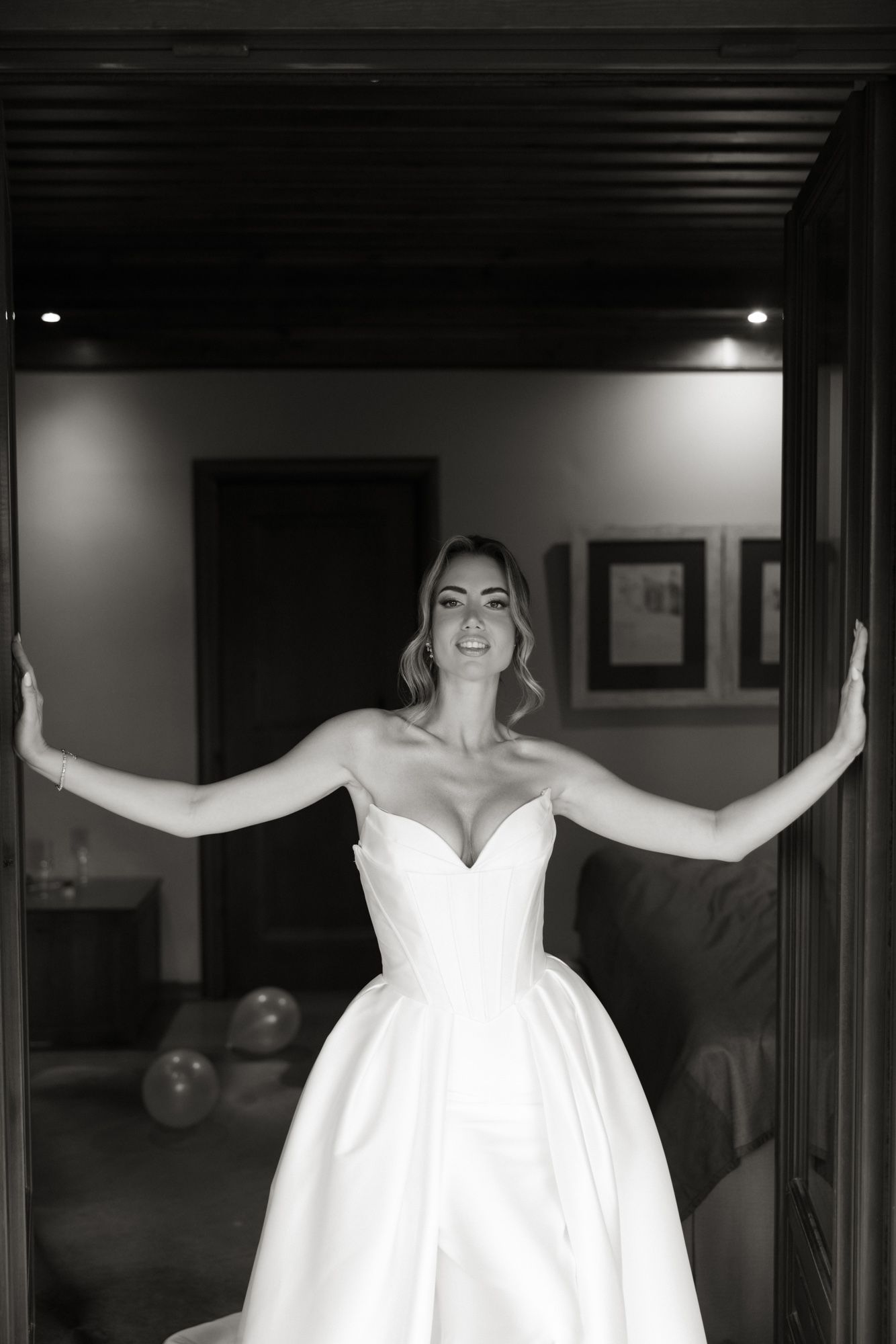 Black and white portrait of a smiling bride in a strapless ball gown standing in a doorway.