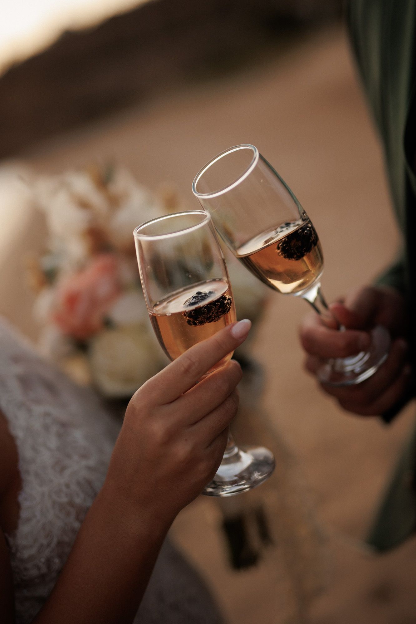 Newlyweds toast with rose champagne glasses with blackberries at beach wedding reception.