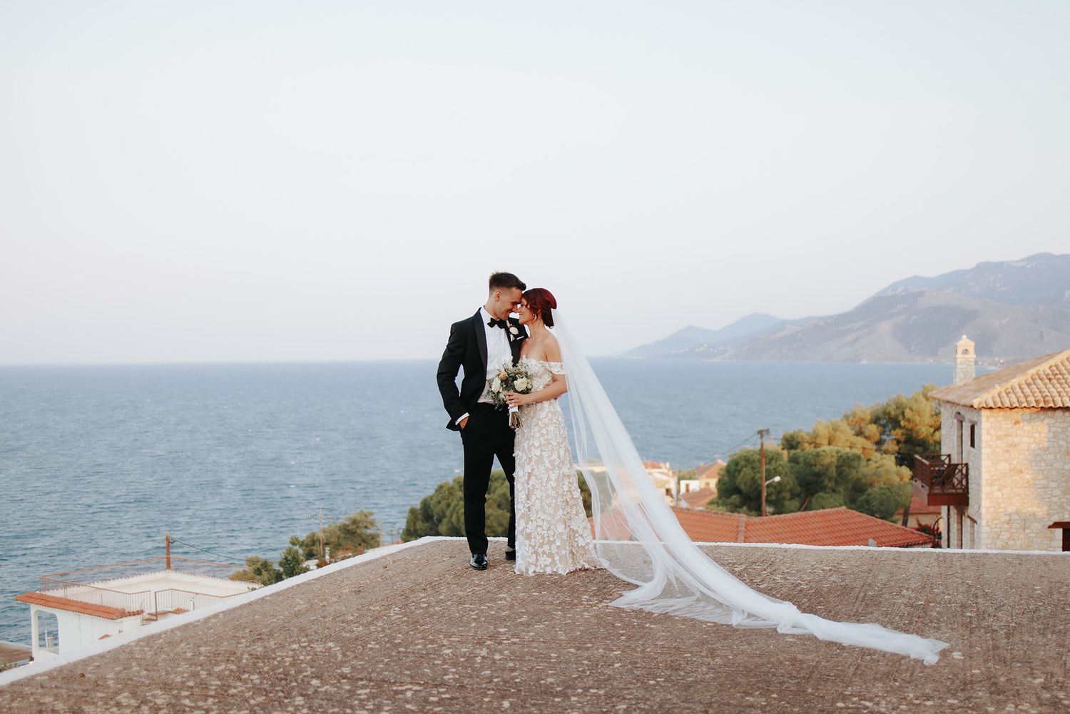 Bride and groom share romantic moment on rooftop overlooking Mediterranean sea and mountains on their wedding day.