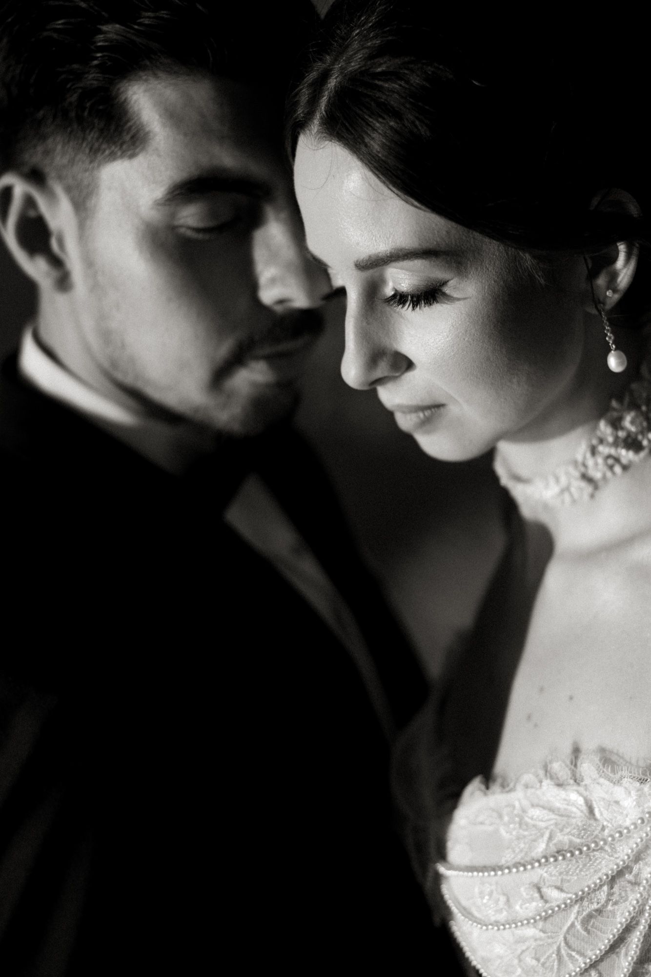 Black and white wedding portrait of bride and groom in intimate close-up, bride wearing lace gown and pearl earrings.