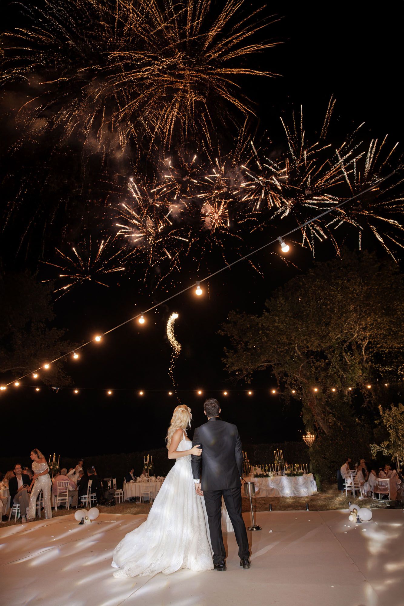 Bride and groom watching spectacular fireworks display at outdoor wedding reception.