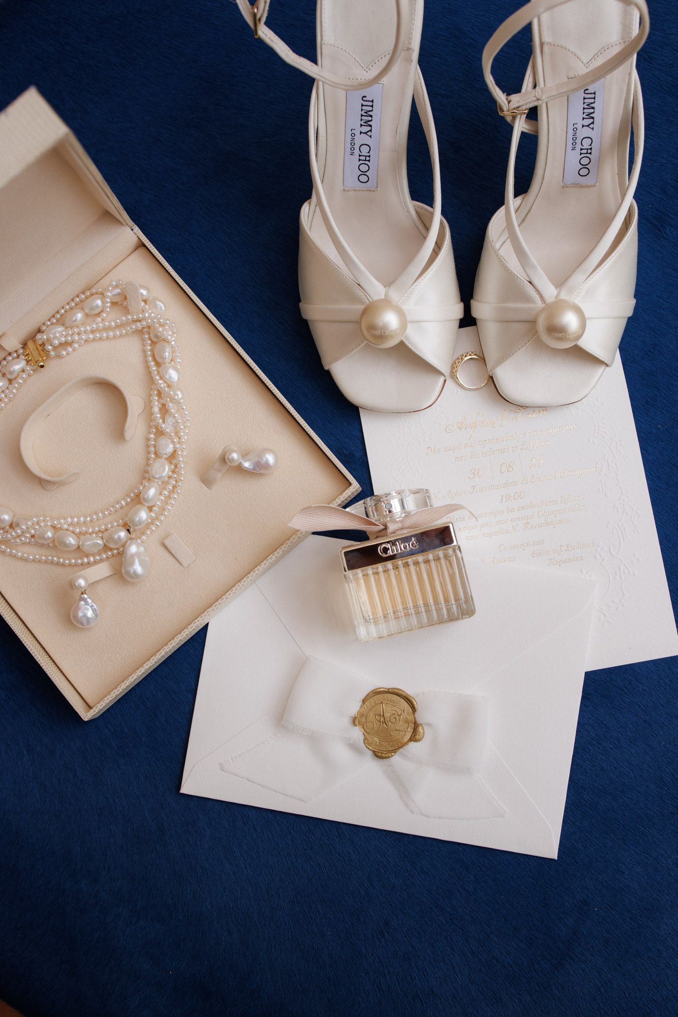 Jimmy Choo bridal heels with pearl detail beside Chloe perfume, pearl jewelry, and wedding invitation.