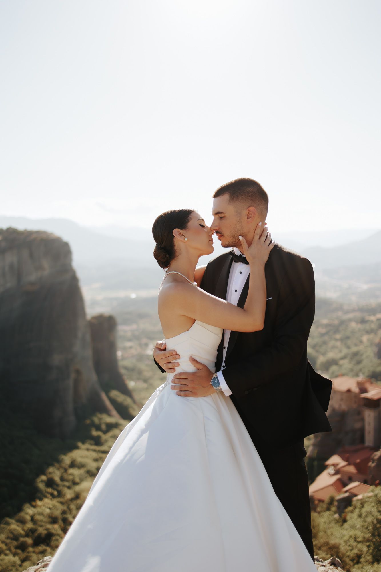 Bride and groom share a romantic moment at Meteora, Greece, with stunning rock formations and valley views in the background.