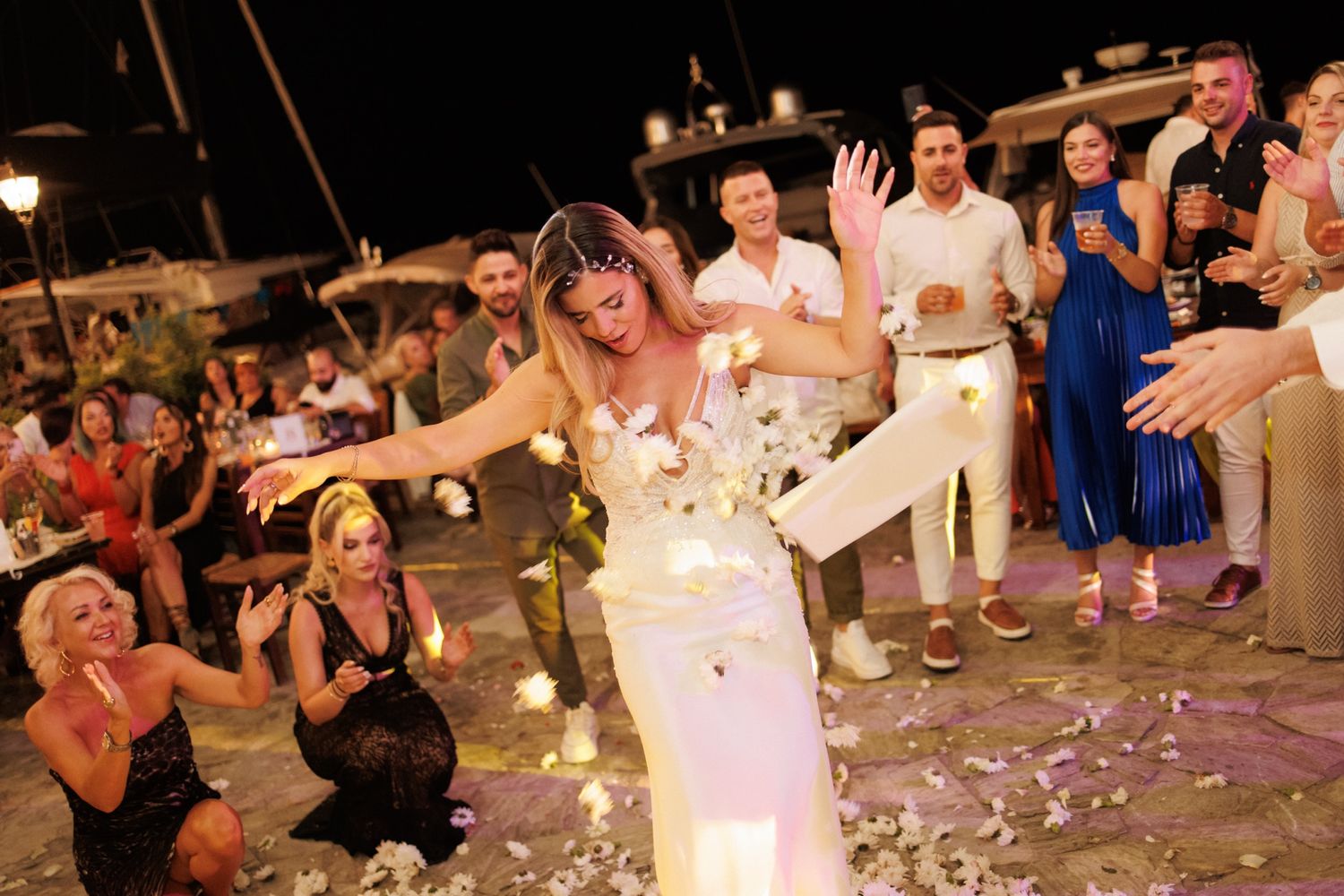 Bride dances joyfully as guests shower her with flower petals at outdoor wedding celebration.