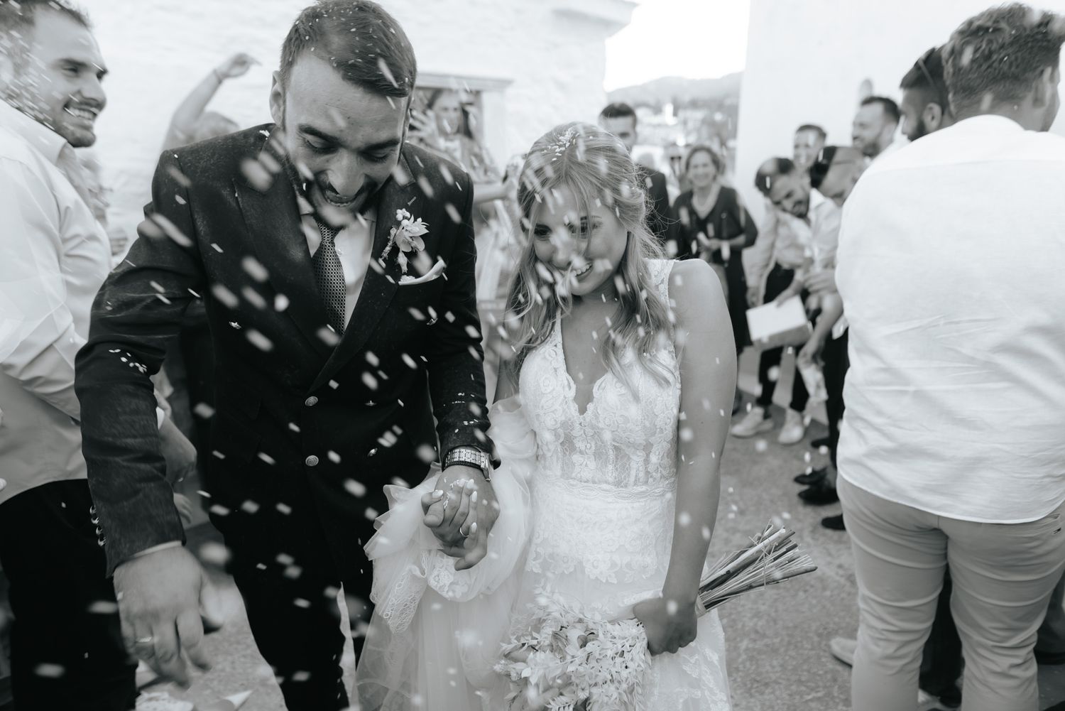Black and white photo of newlyweds walking through a shower of confetti after their wedding ceremony.