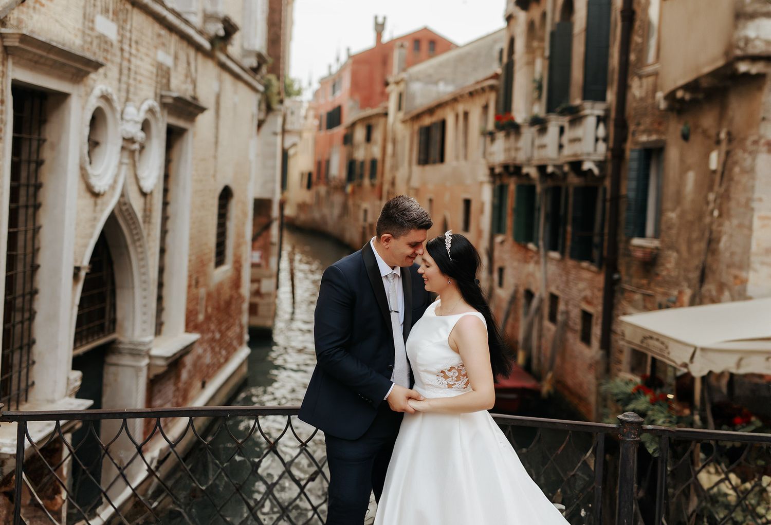 Romantic couple embraces on a bridge overlooking a scenic Venice canal with historic architecture in the background.