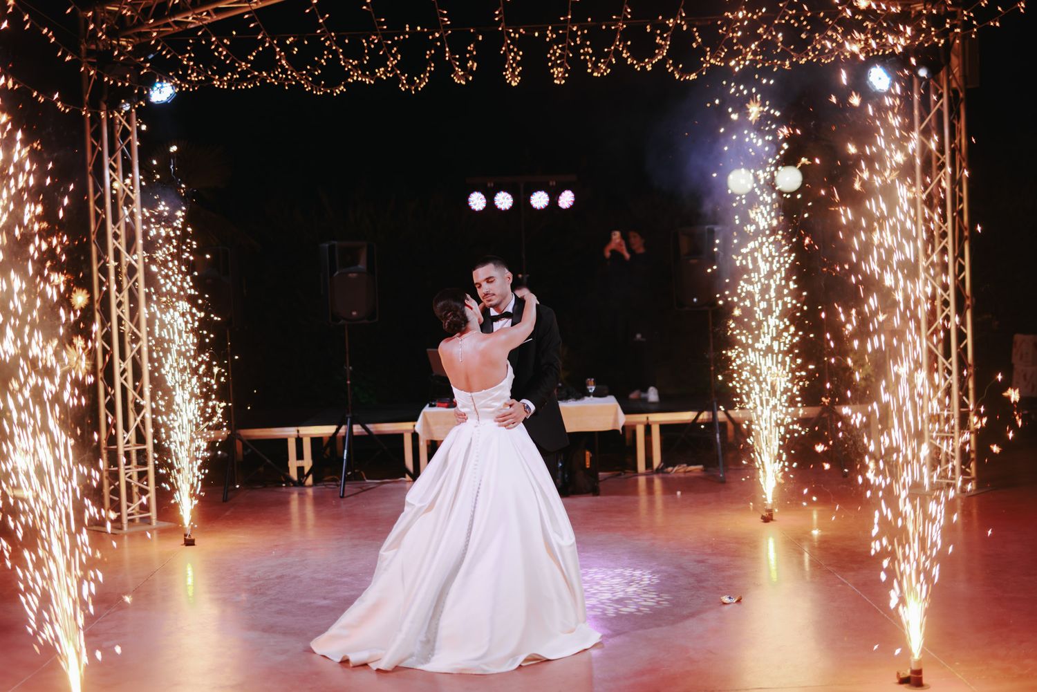 Bride and groom share first dance surrounded by sparkling fountain fireworks at elegant wedding reception.
