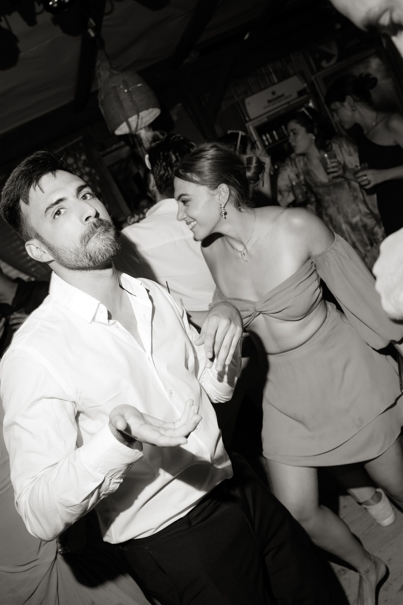 Black and white photo of couple dancing closely together at crowded wedding reception.