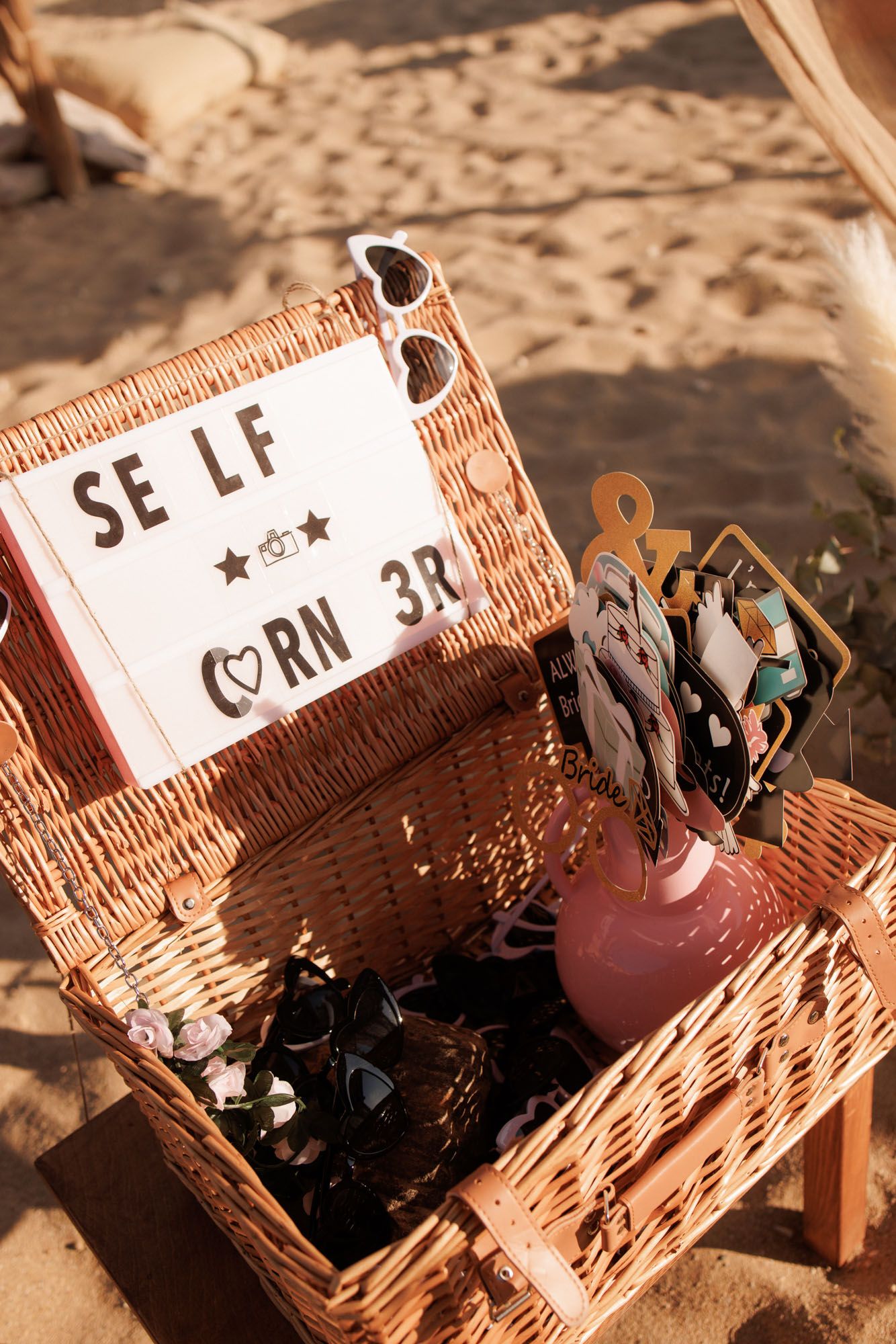 Wicker basket selfie corner station with fun props and signs at beach wedding.