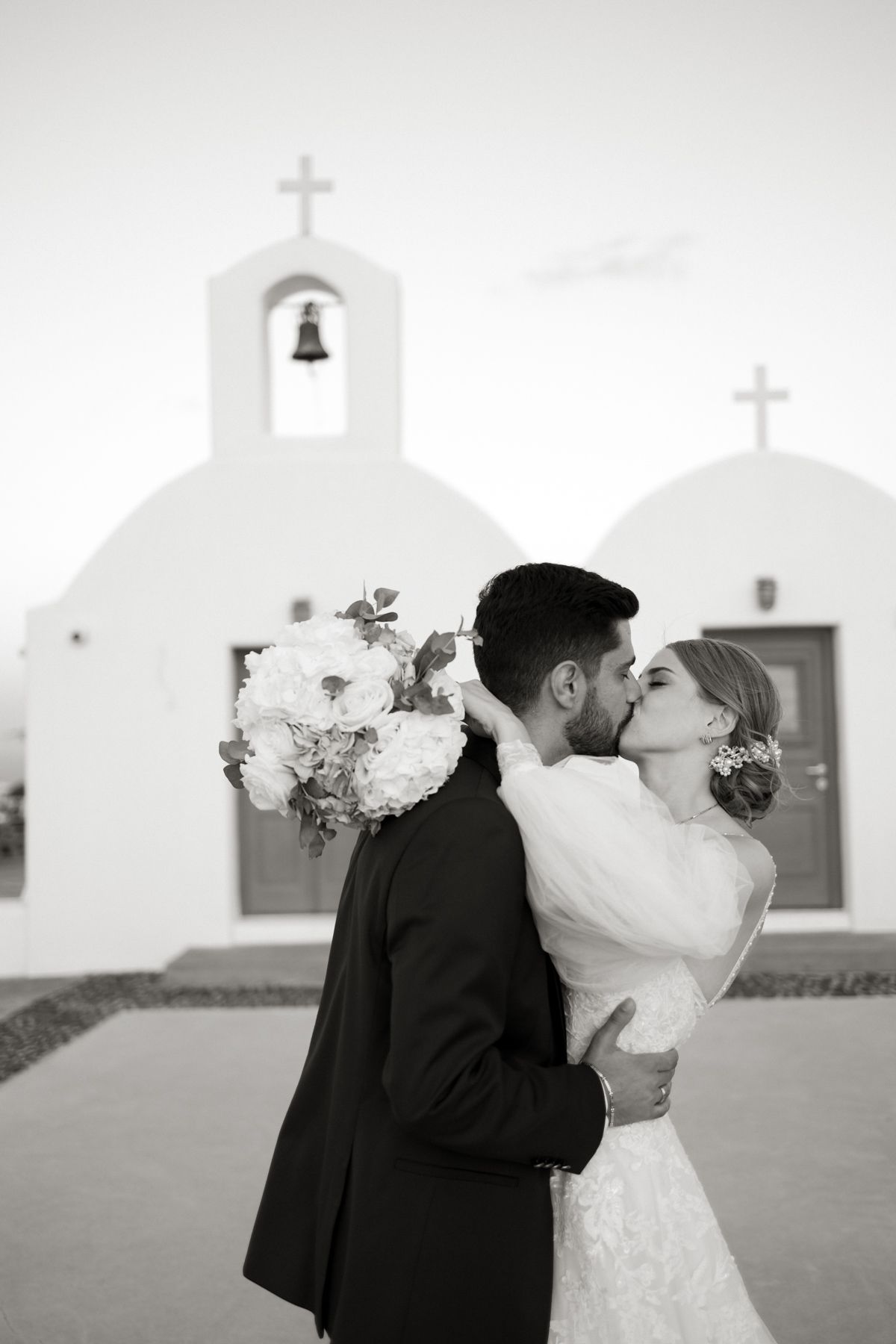 Bride and groom share a kiss in front of a white Greek Orthodox chapel in Santorini.