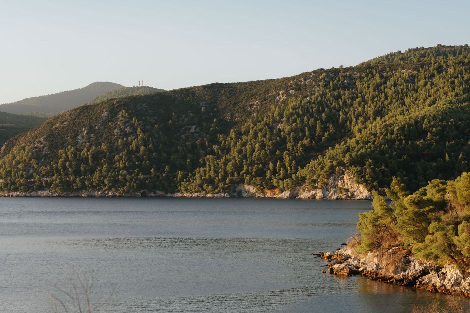 Serene bay surrounded by lush green forested hills reflecting on calm blue waters at golden hour.
