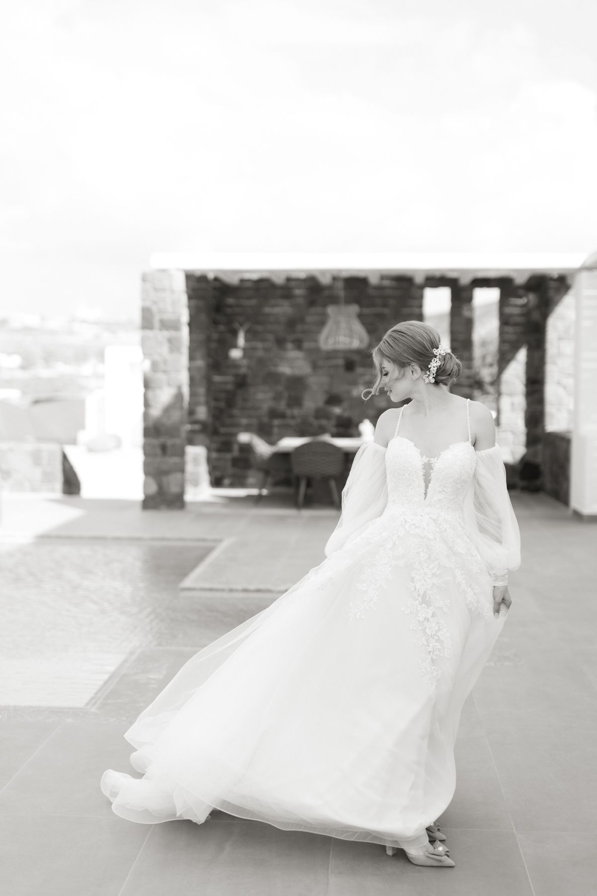 Black and white photo of a bride in a flowing lace gown with sheer sleeves walking on a villa terrace.