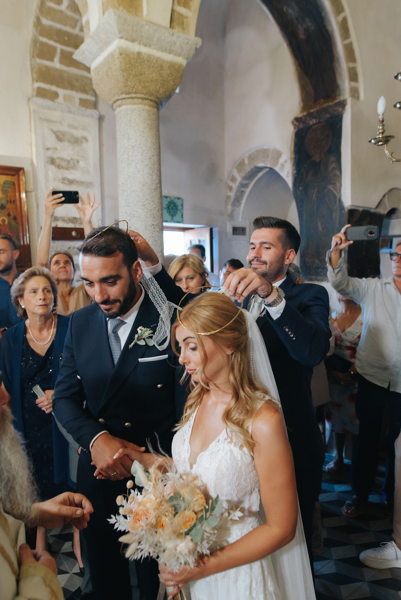 Orthodox wedding ceremony with bride and groom receiving stefana crowns inside historic church.