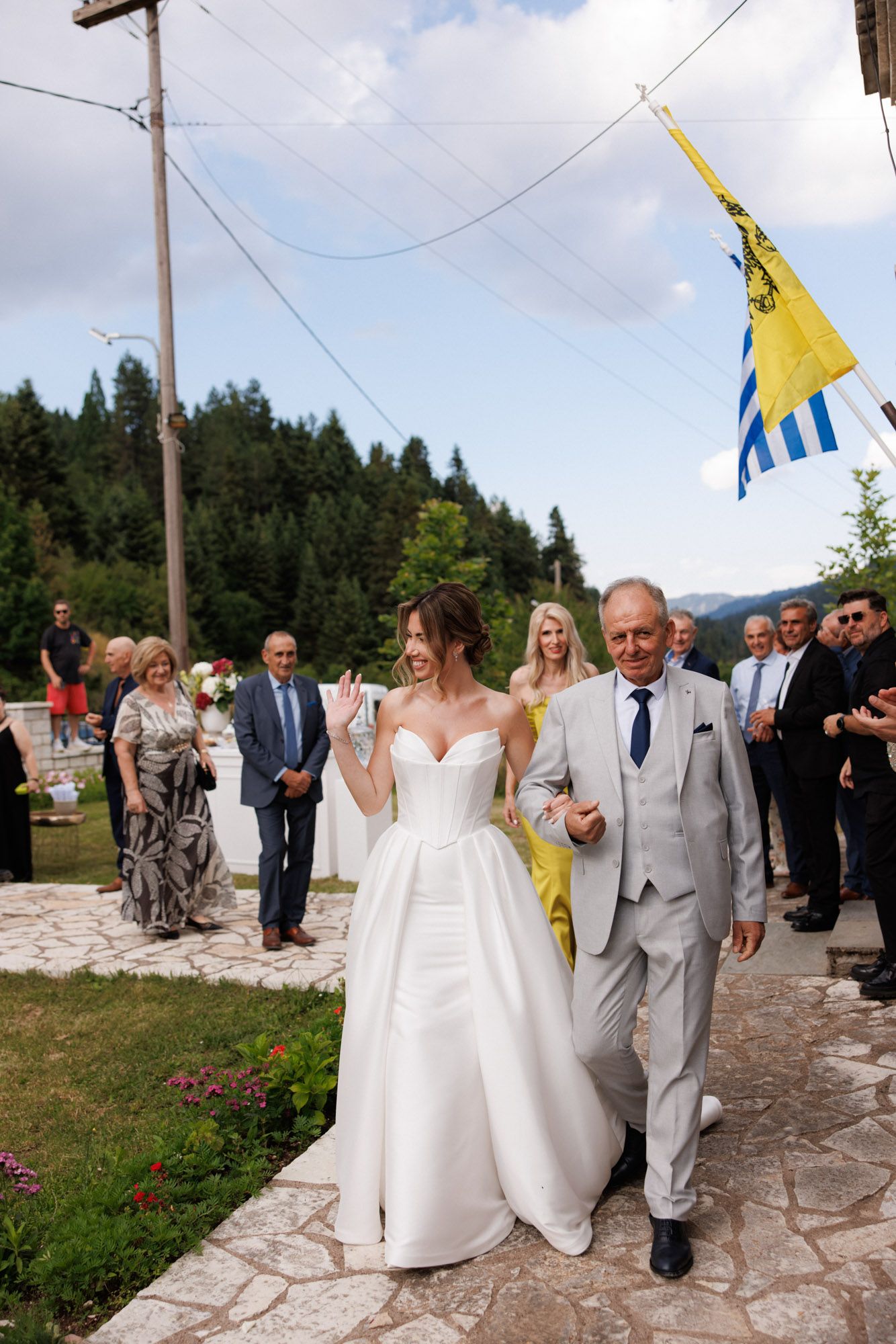 Bride in strapless white gown walking with her father outside a Greek Orthodox church.