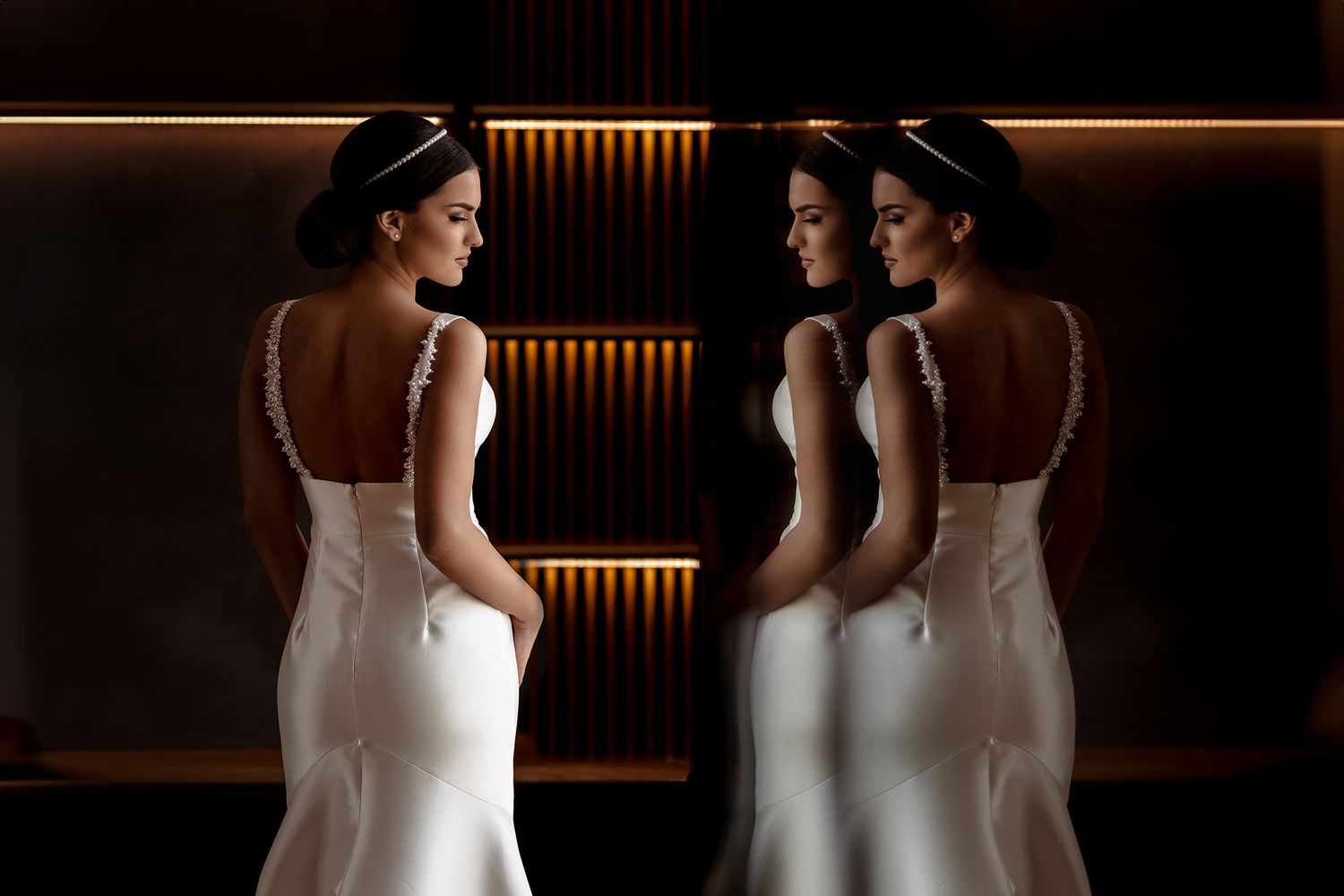 Elegant bridal portrait showing reflection in mirrors with warm lighting and fitted white wedding dresses.
